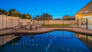 A swimming pool with a curved edge, surrounded by a fence and outdoor seating.