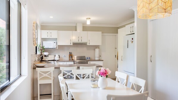 A modern kitchen with white cabinets, a built-in oven, and a dining area with a white table and chairs.