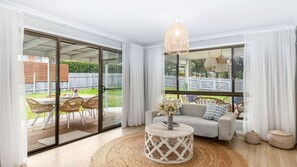A spacious living room with a sliding glass door leading to a patio, a round coffee table, and a large window with curtains.