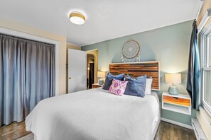 Habitación de hotel con una cama grande, una mesita de noche con lámpara, un atrapasueños colgando en la pared y vistas al exterior.