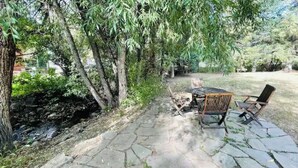 Eine Terrassengruppe im Freien mit einem Steintisch und Stühlen, umgeben von Bäumen und einer Steinmauer.