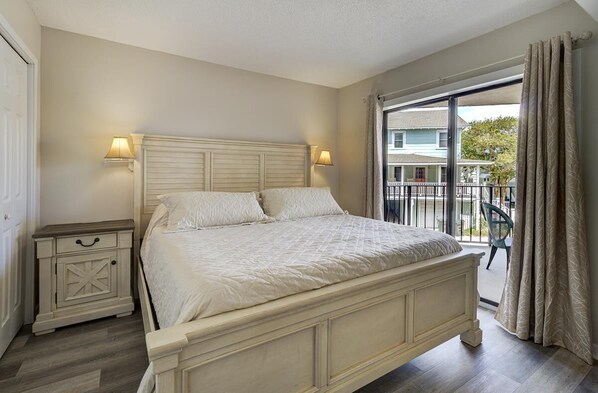 A bedroom with a large bed, bedside lamps, a nightstand, and a balcony with a view of the outside.