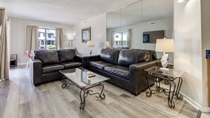 A modern living room with leather sofas, a glass coffee table, and a large mirror. - Ocean Views, Balcony, Pool, STEPS to Beach, Restaurants, Shops (Wrightsville Beach)