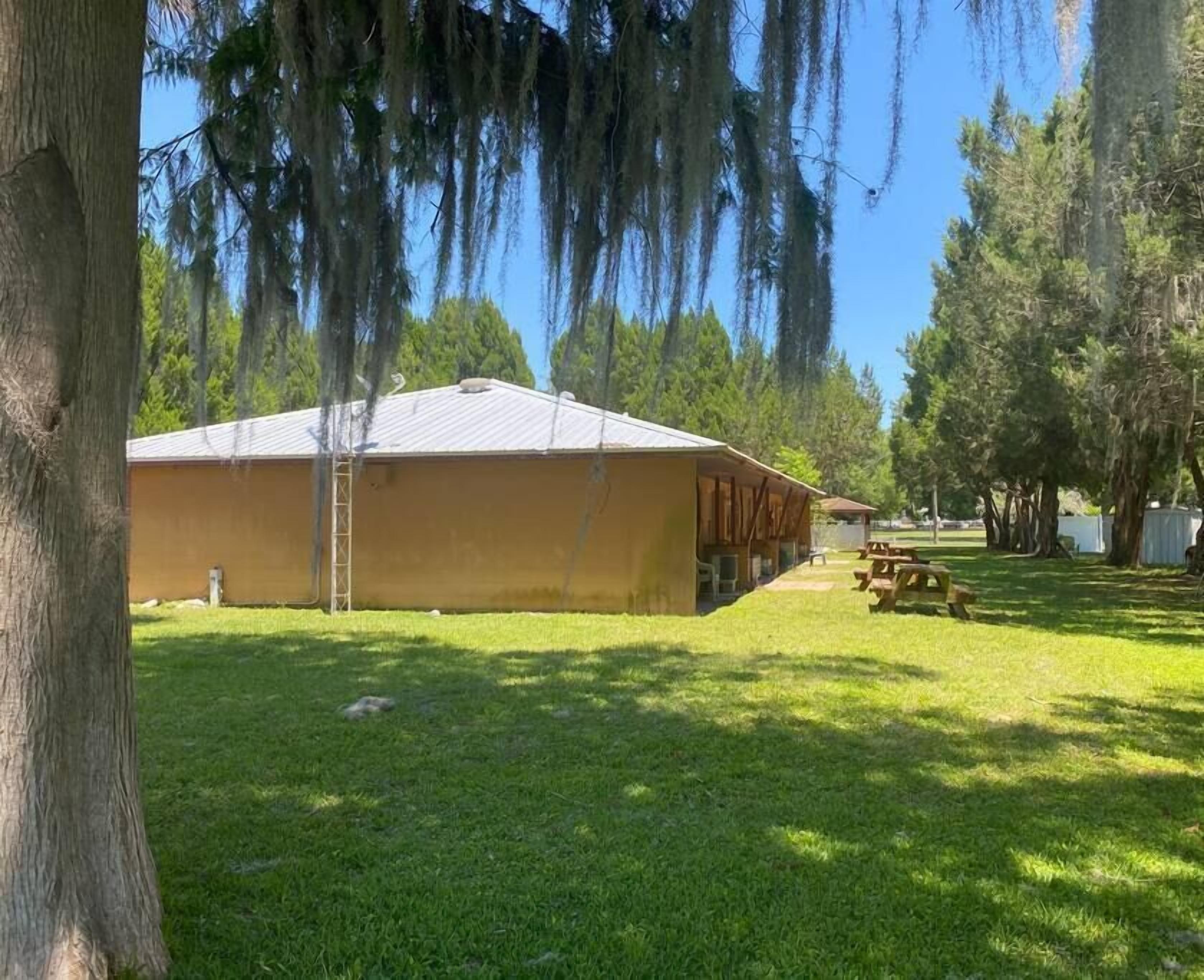 Un bâtiment jaune doté d’un porche abrité, entouré d’arbres et agrémenté d’une table de pique-nique.