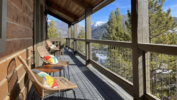 A wooden deck with wicker chairs and a table, overlooking a mountainous landscape. - Midcentury Mountain Cabin, complete with hot tub, game room and amazing VIEWS!! (Grand Lake)