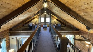 An attic room with a wooden sloped ceiling, a central light fixture, a staircase, and a view of the lower level. - Midcentury Mountain Cabin, complete with hot tub, game room and amazing VIEWS!! (Grand Lake)