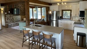 A modern kitchen with a central island, bar stools, a stone accent wall, and a built-in oven. - Midcentury Mountain Cabin, complete with hot tub, game room and amazing VIEWS!! (Grand Lake)