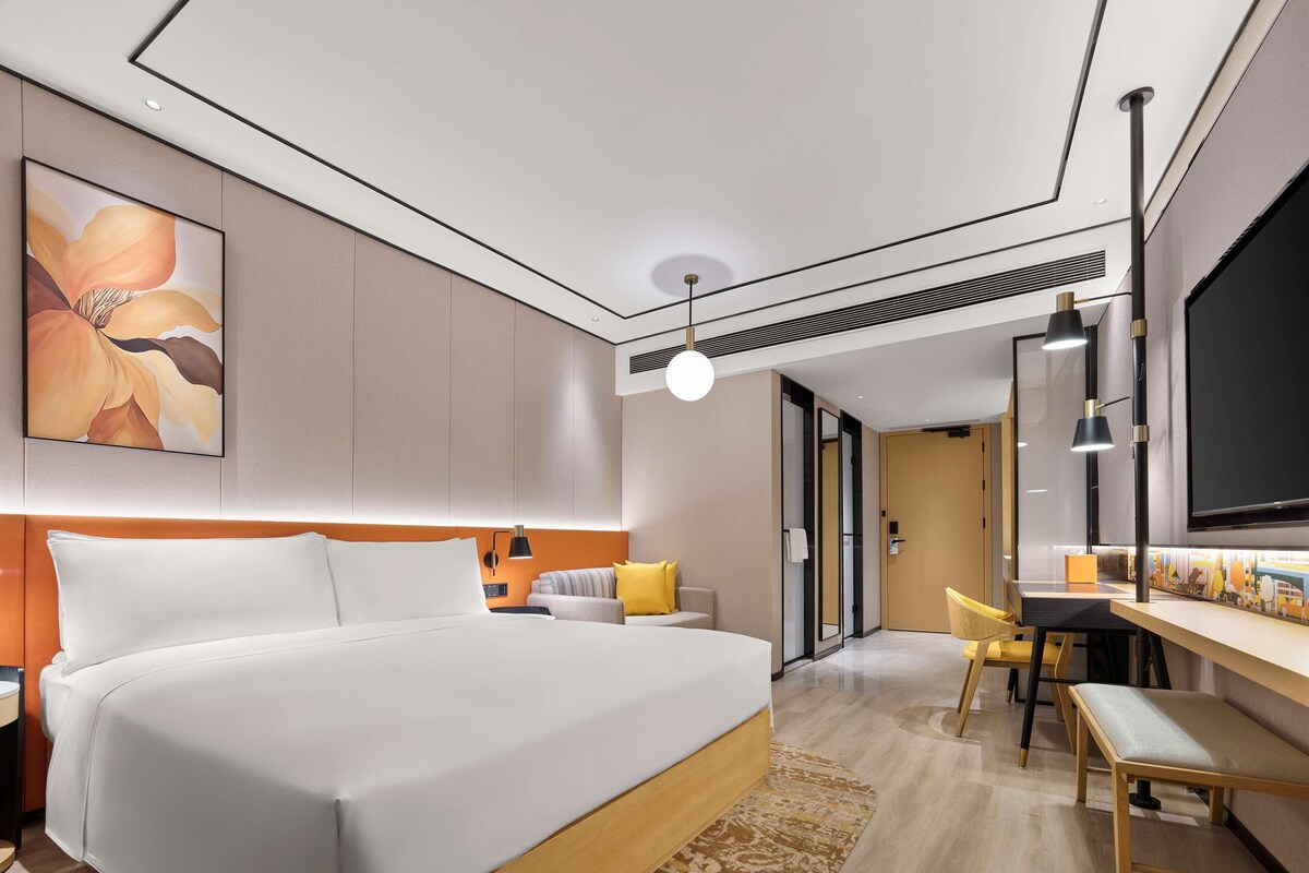 A modern hotel room with a large bed, a desk, a chair, and a television.