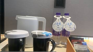 A coffee station with two black mugs, a white coffee pot, and two bottles of water with purple caps.