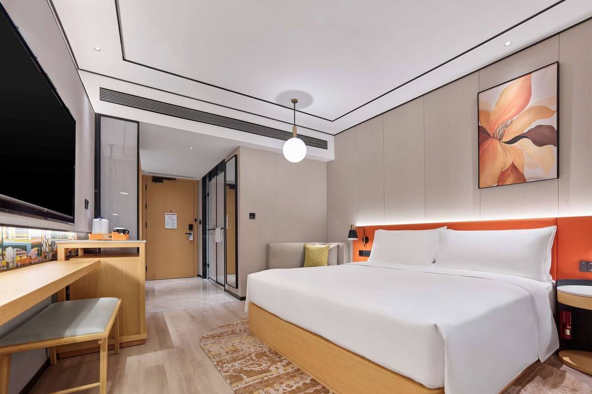 A modern hotel room with a large bed, a desk, and a television.