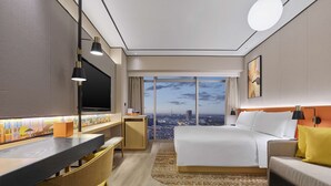 A modern hotel room with a large bed, a desk with a chair, a TV, and a view of the cityscape. - Hilton Garden Inn Anshan Haicheng (Anshan)