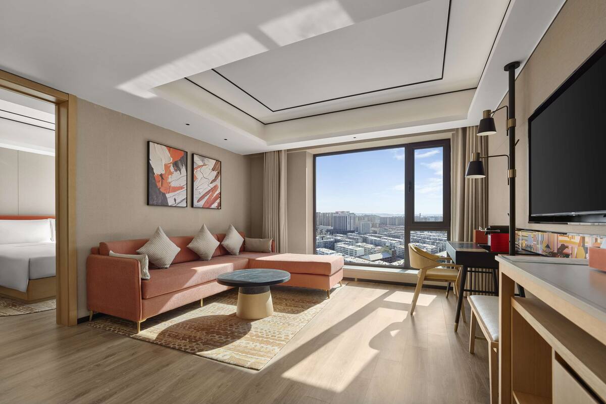 A modern living room with a sofa, coffee table, and a large window offering a city view.