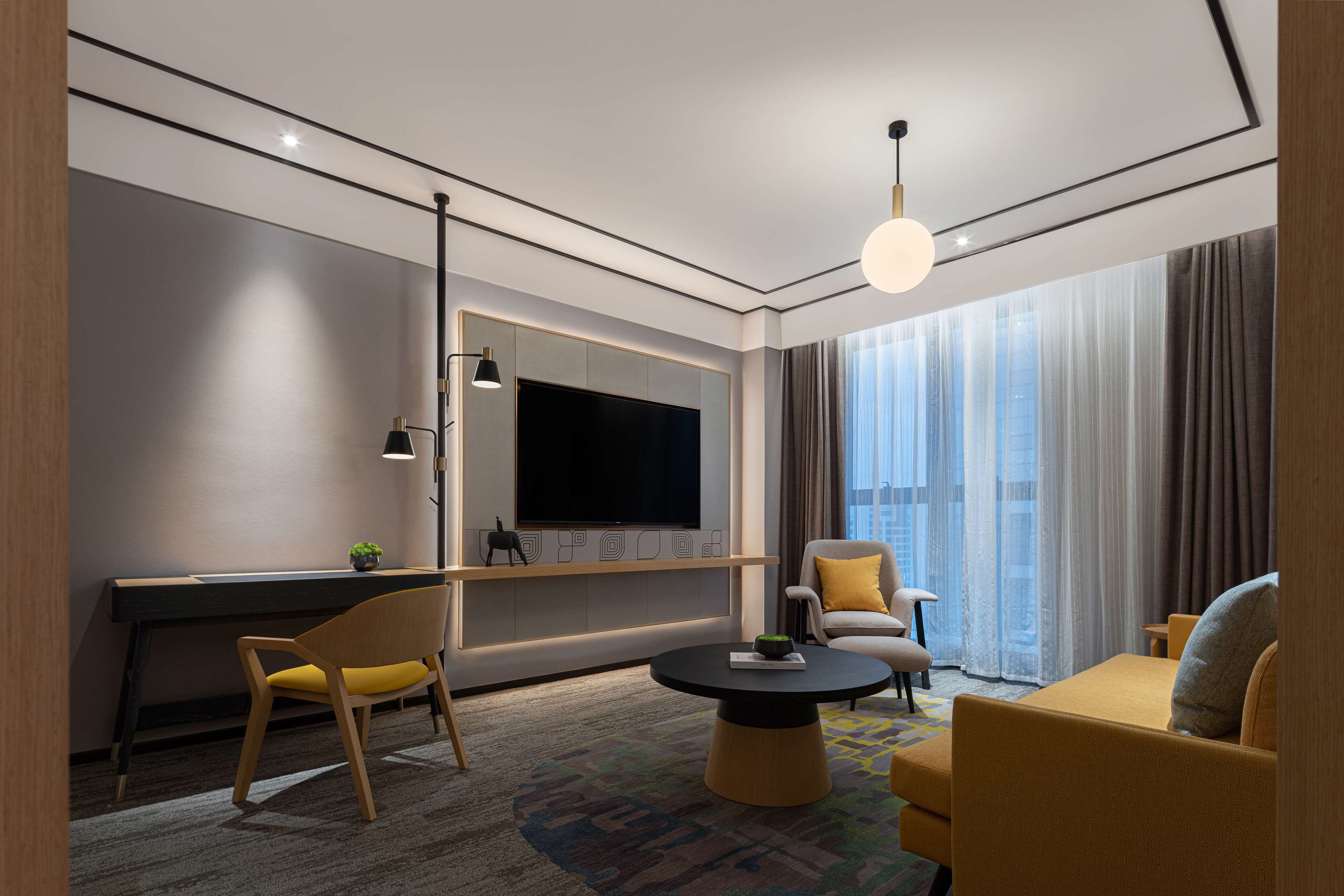 Ett modernt hotellrum med en stor platt-TV, en soffa, en fåtölj och ett skrivbord.