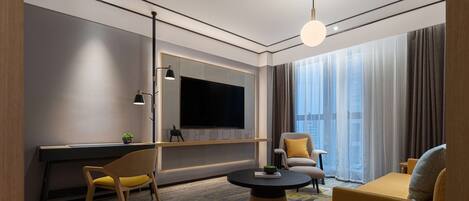 A modern hotel room with a large flat-screen TV, a sofa, a chair, and a desk.