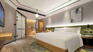 A modern hotel room with a large bed, bedside tables, a wall-mounted artwork, and a carpeted floor.