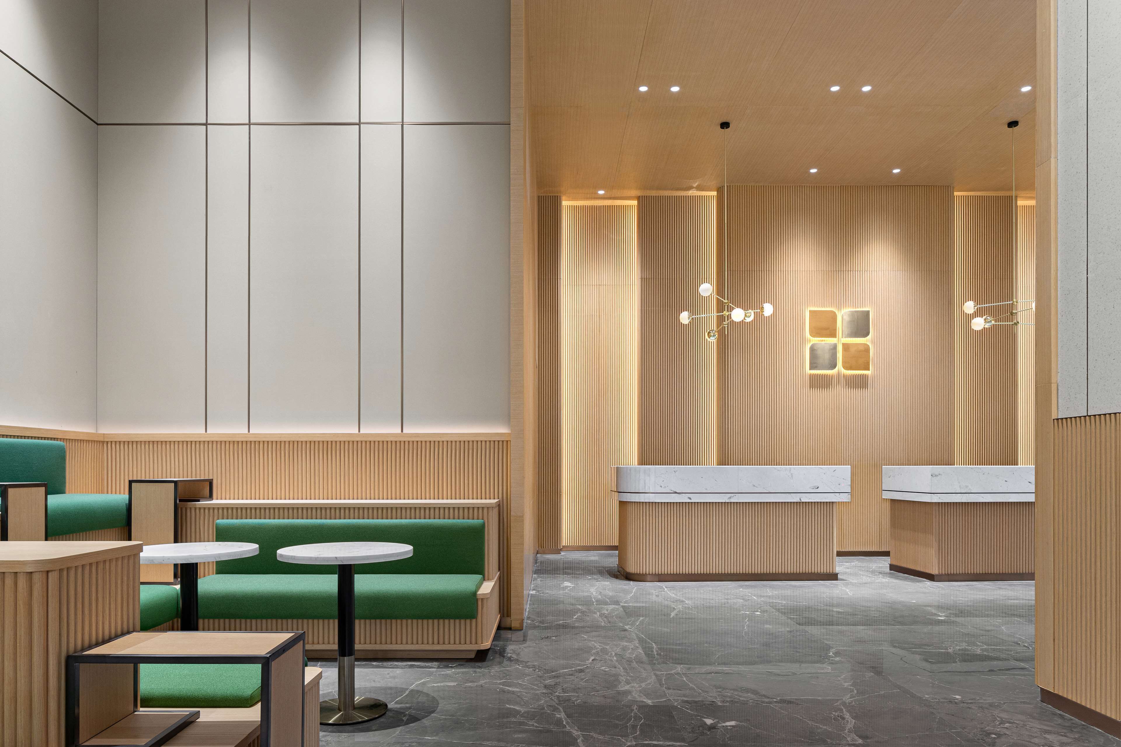 A modern interior with green seating, white tables, and a reception area with a wooden finish.