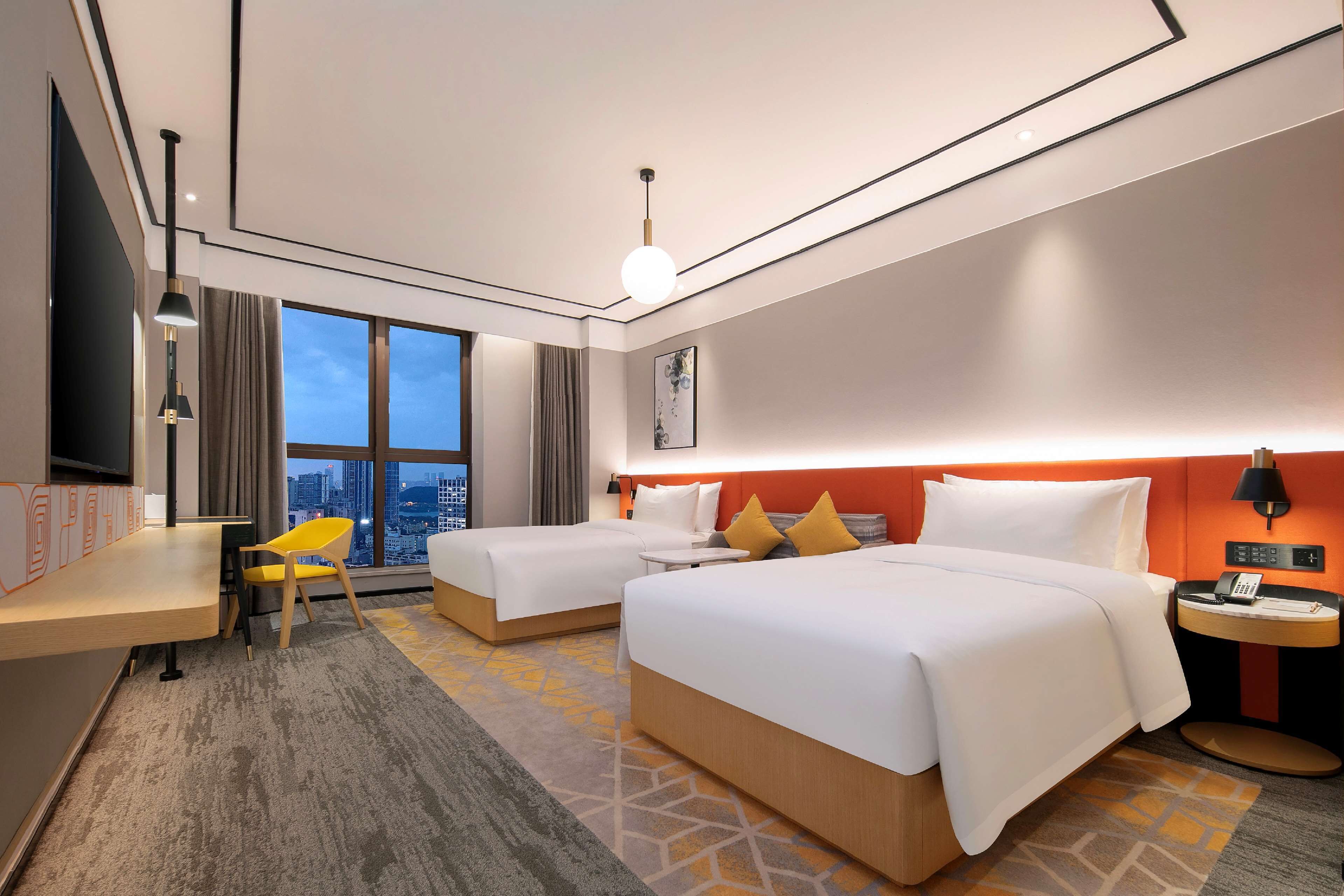 A hotel room with two beds, a desk, a chair, a nightstand, and a large window with a city view.