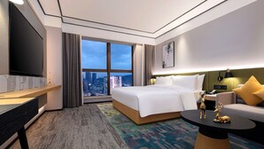 Habitación de hotel con una cama grande, televisión, escritorio, sofá y vista a la ciudad.