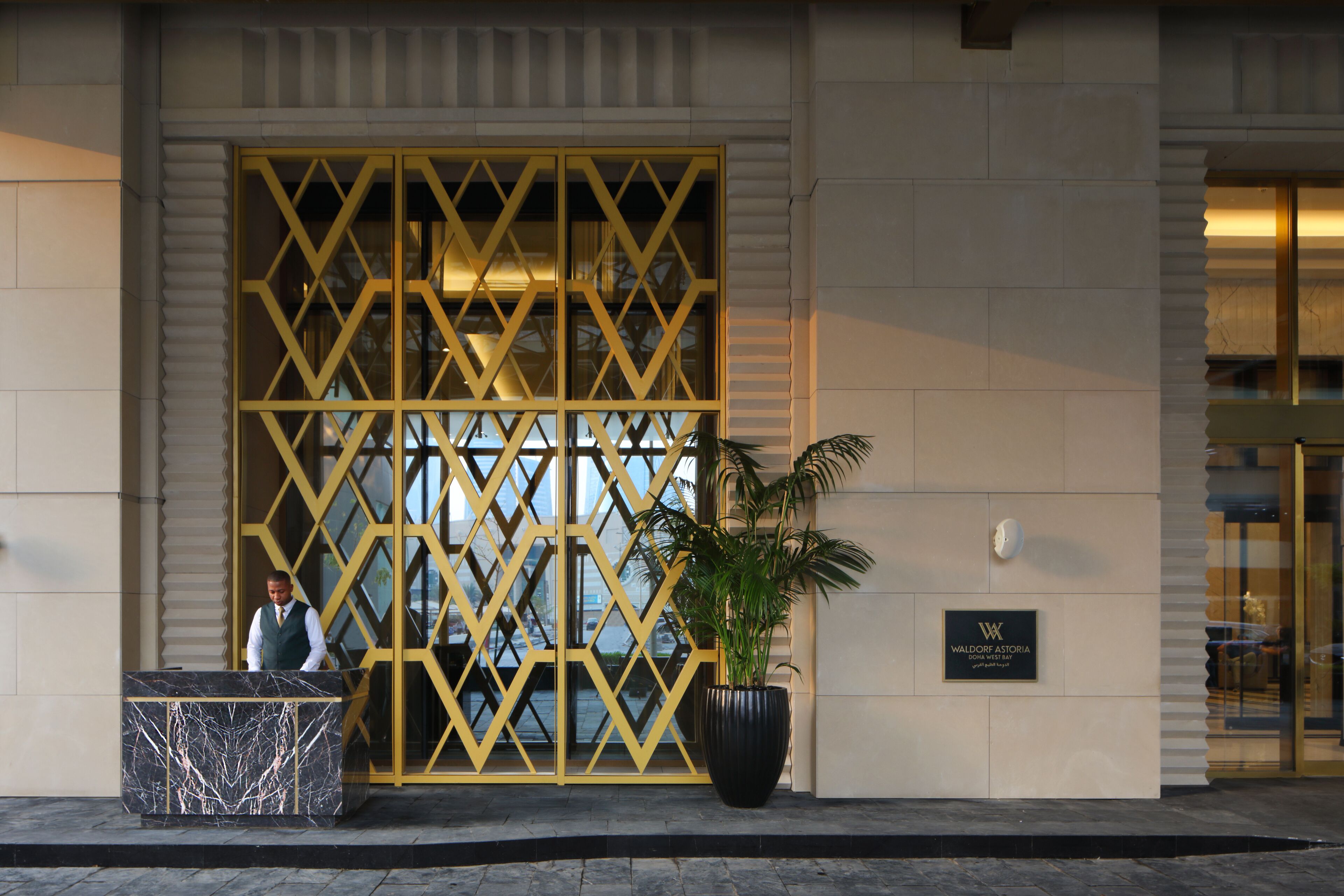 A hotel entrance with a reception desk, a large potted plant, and a decorative yellow gate.