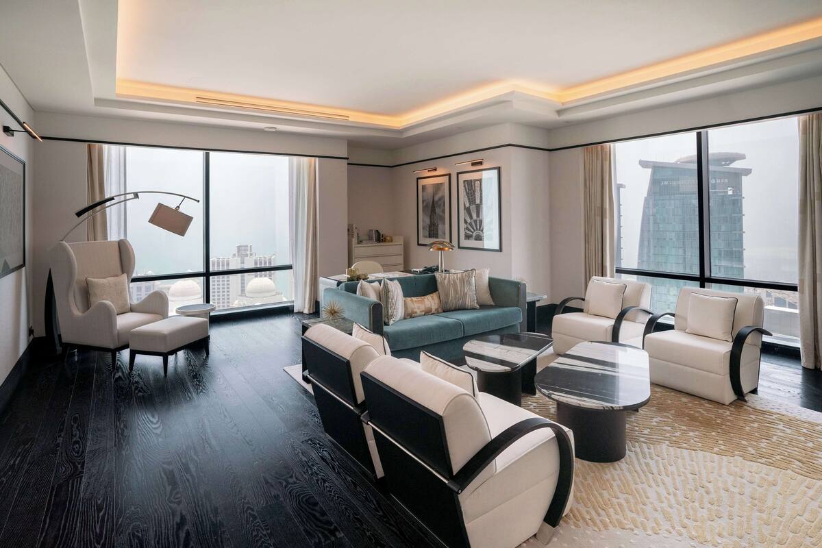 Une chambre d’hôtel moderne avec un parquet en bois foncé, un ensemble de canapés, une table basse et une grande fenêtre donnant sur la ville.