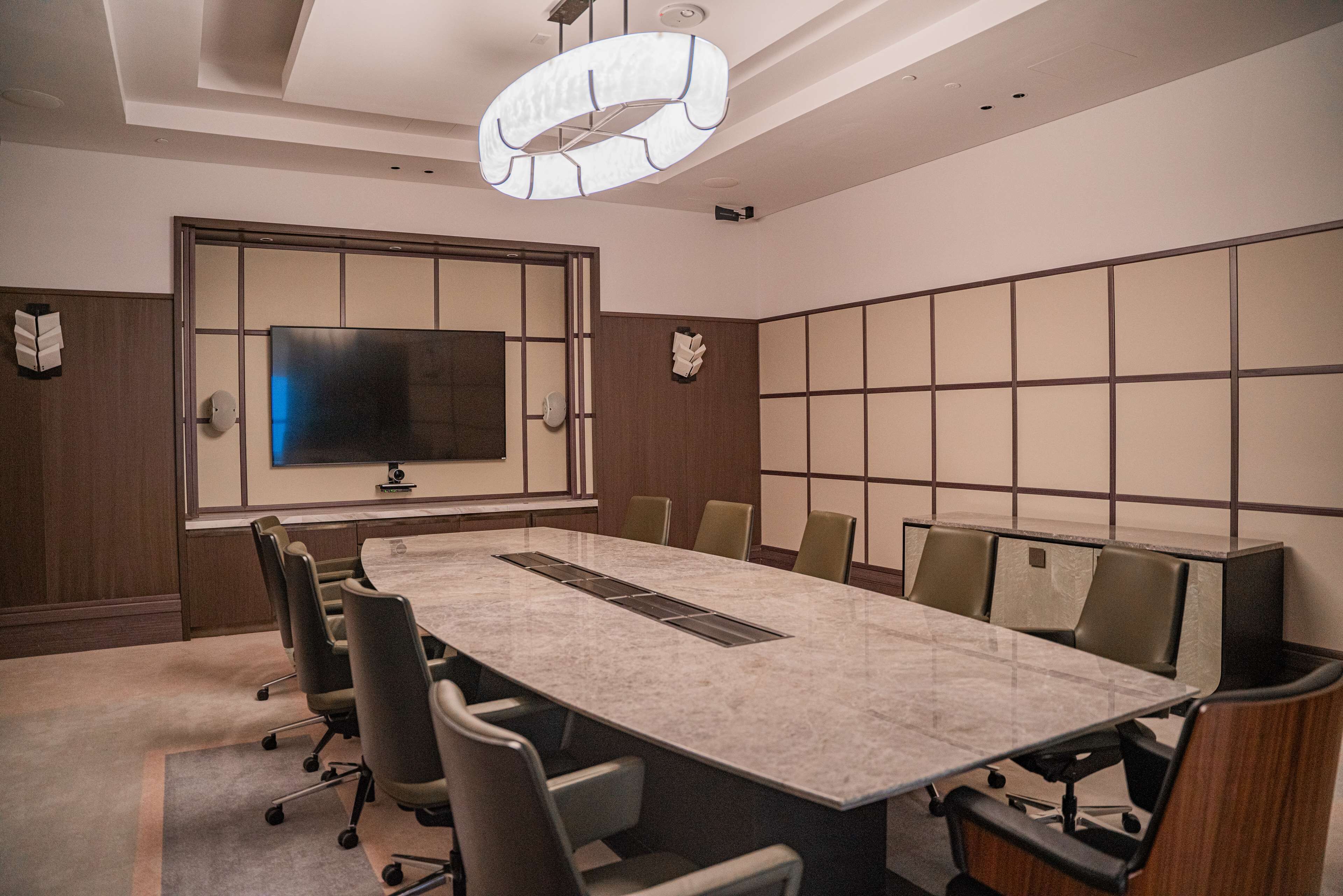 Une salle de conférence équipée d’une grande table, de chaises, d’un téléviseur à écran plat et d’un panneau mural de style japonais traditionnel.