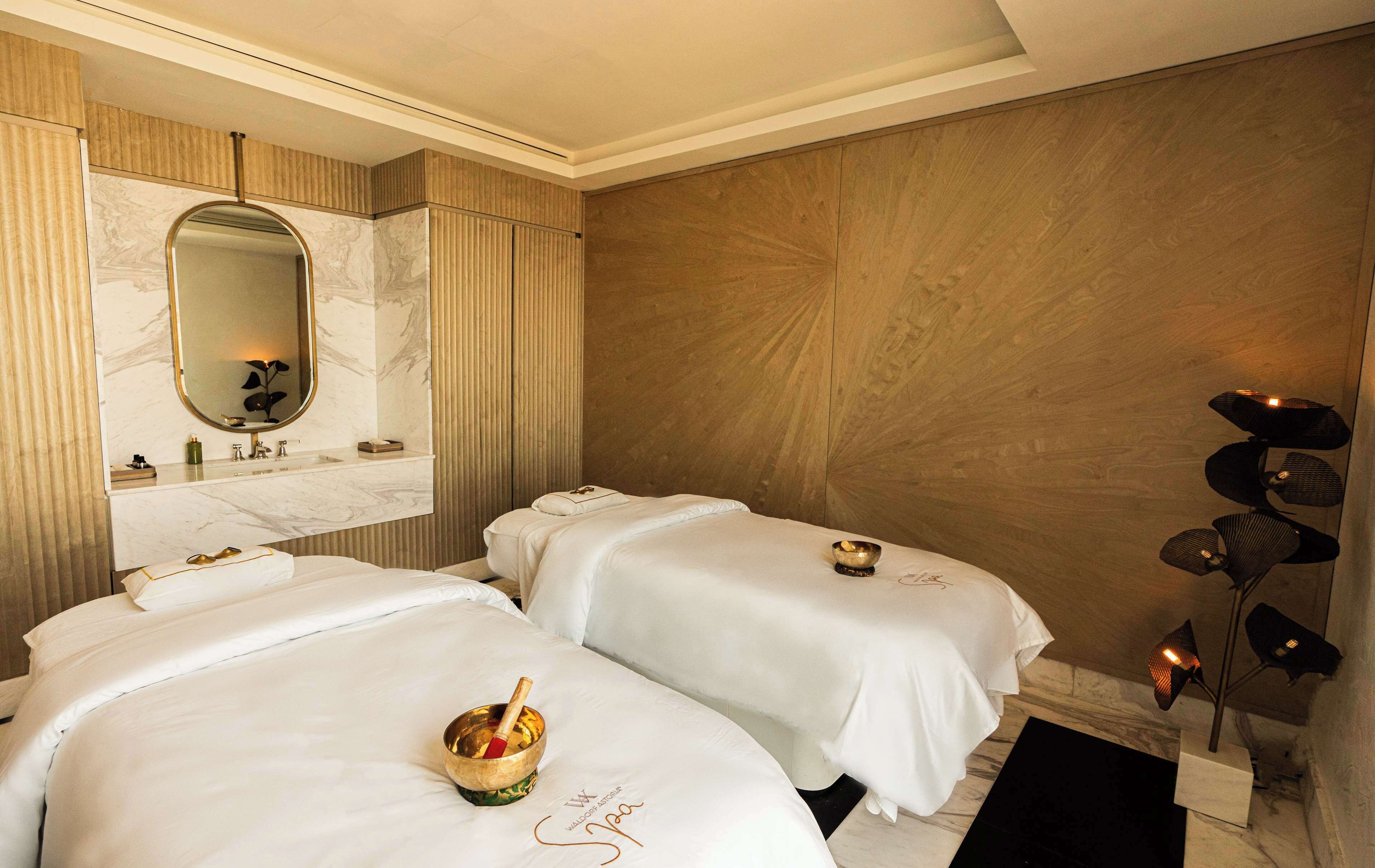 Habitación de hotel con dos camas, un tocador de mármol y una mesa de masajes.