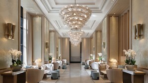 A luxurious hotel lobby with a central chandelier, plush seating, and decorative plants.