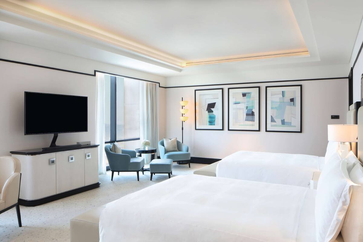 Une chambre d’hôtel équipée d’un lit, d’une télévision, d’un bureau, d’une chaise et d’œuvres d’art accrochées au mur.