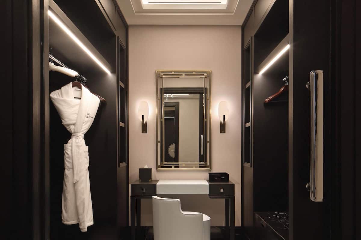 Une salle de bain moderne avec un grand miroir, un peignoir suspendu à un porte-manteau, un lavabo rond blanc et un sol foncé.