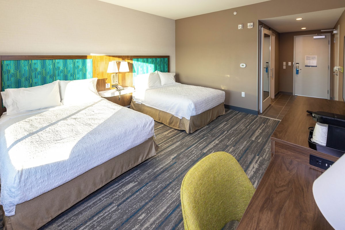 Ein Hotelzimmer mit zwei Betten, einem Schreibtisch, einem Stuhl und einer Badezimmertür.