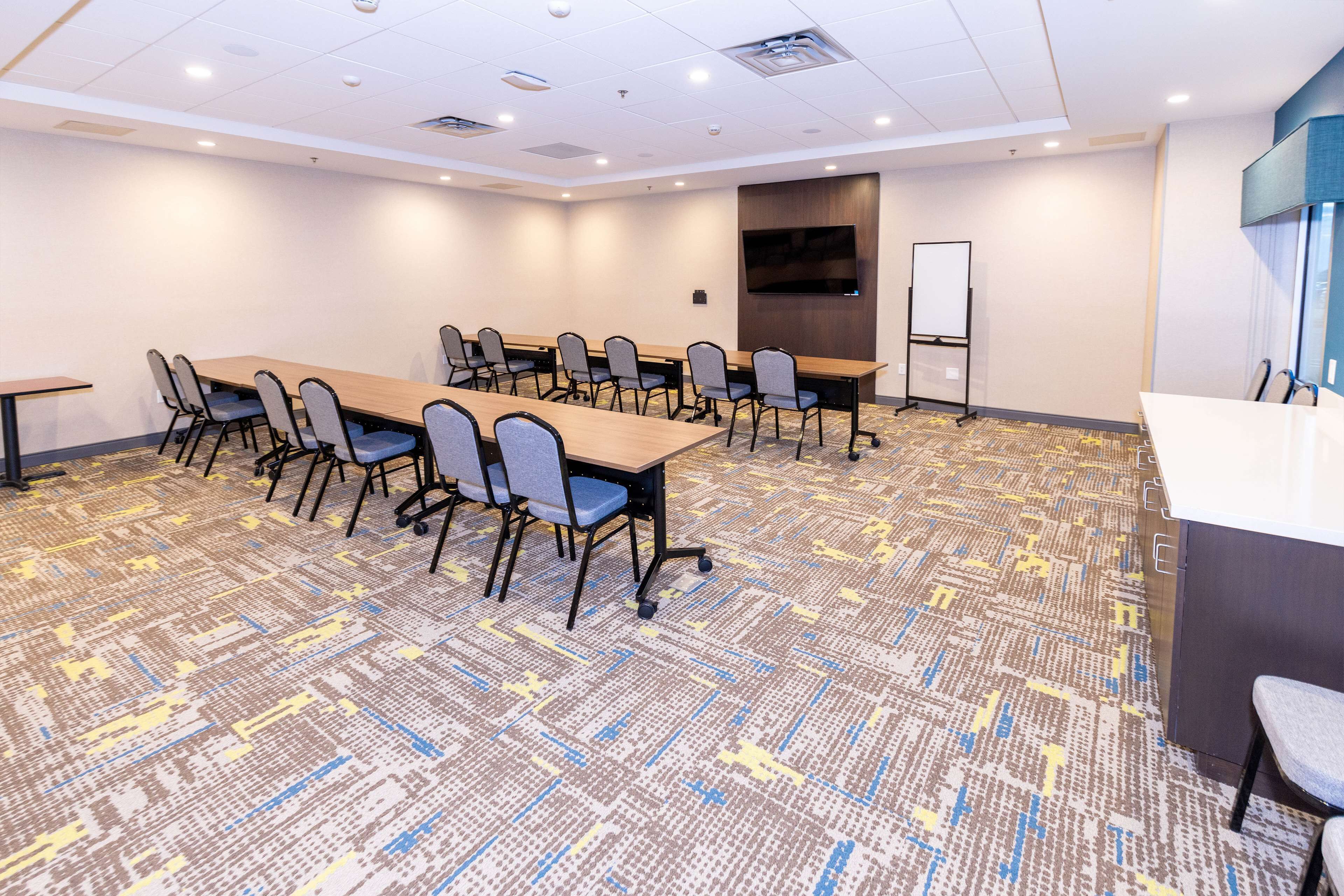 A conference room with a large table, chairs, a whiteboard, and a TV screen.