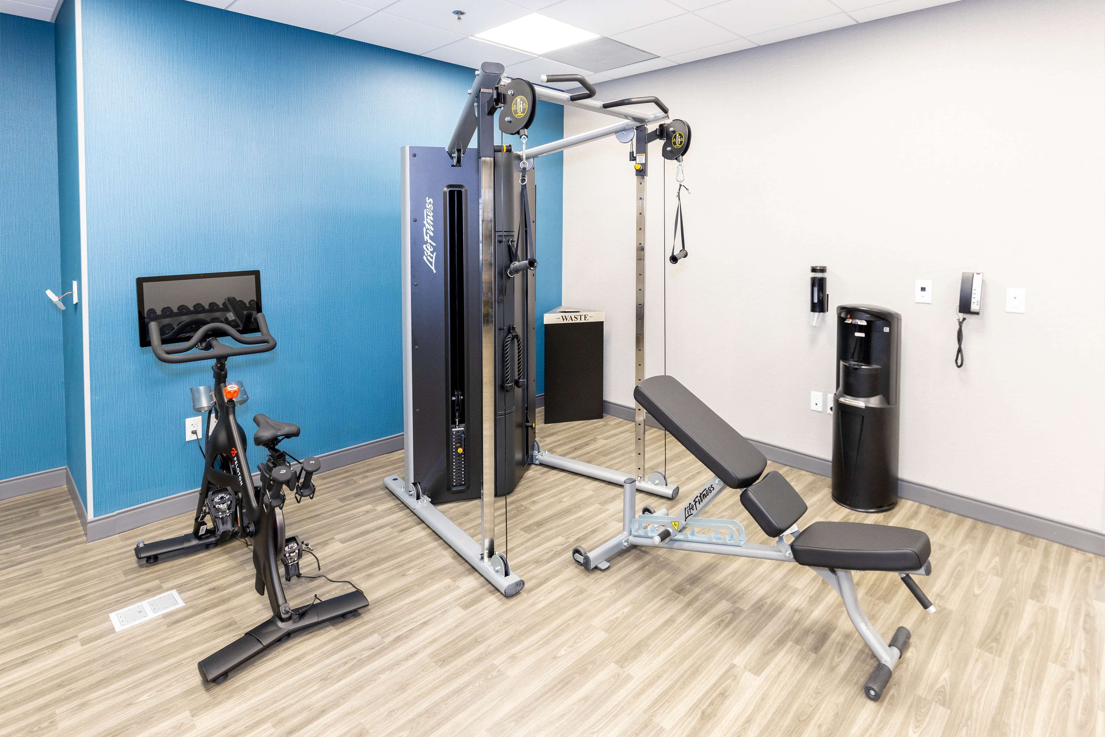 A gym with a weight machine, a bench, and a wall-mounted screen.