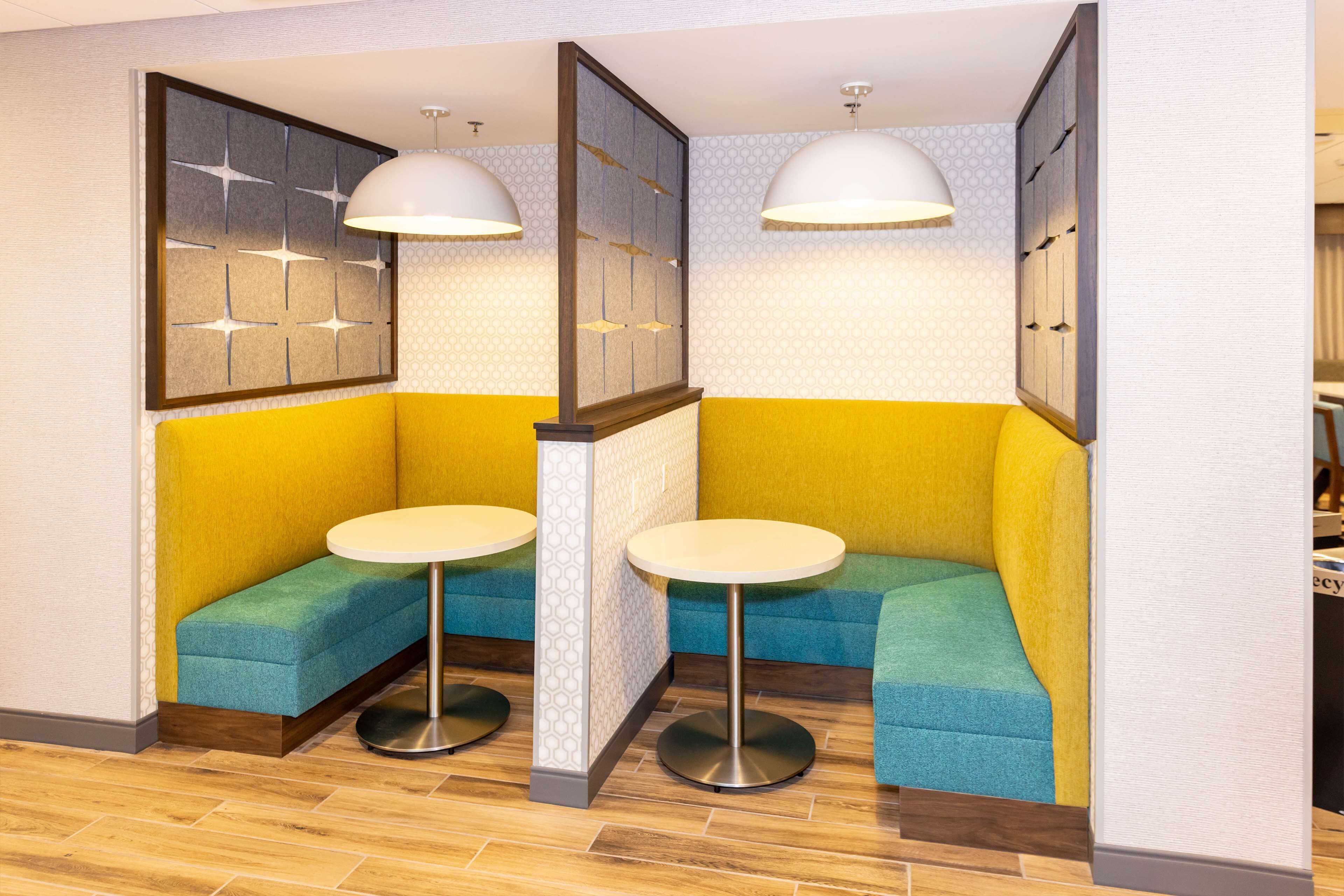 A corner seating area with two round tables and cushioned benches, a decorative wall panel, and pendant lighting.