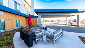 An outdoor seating area with modern furniture, a red umbrella, and a building with a blue and beige facade in the background.