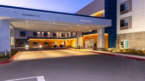 A hotel entrance with a 'Welcome' sign, a covered parking area, and a 'Clearance 13' sign.