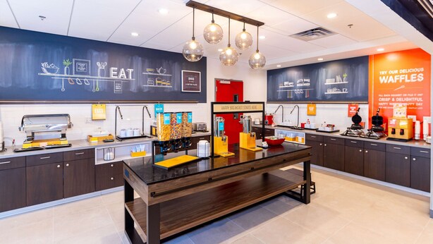 A modern kitchen with a central island, various appliances, and a chalkboard wall with menu options.