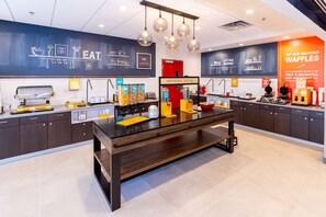 A modern kitchen with a central island, various appliances, and a chalkboard wall with menu options.