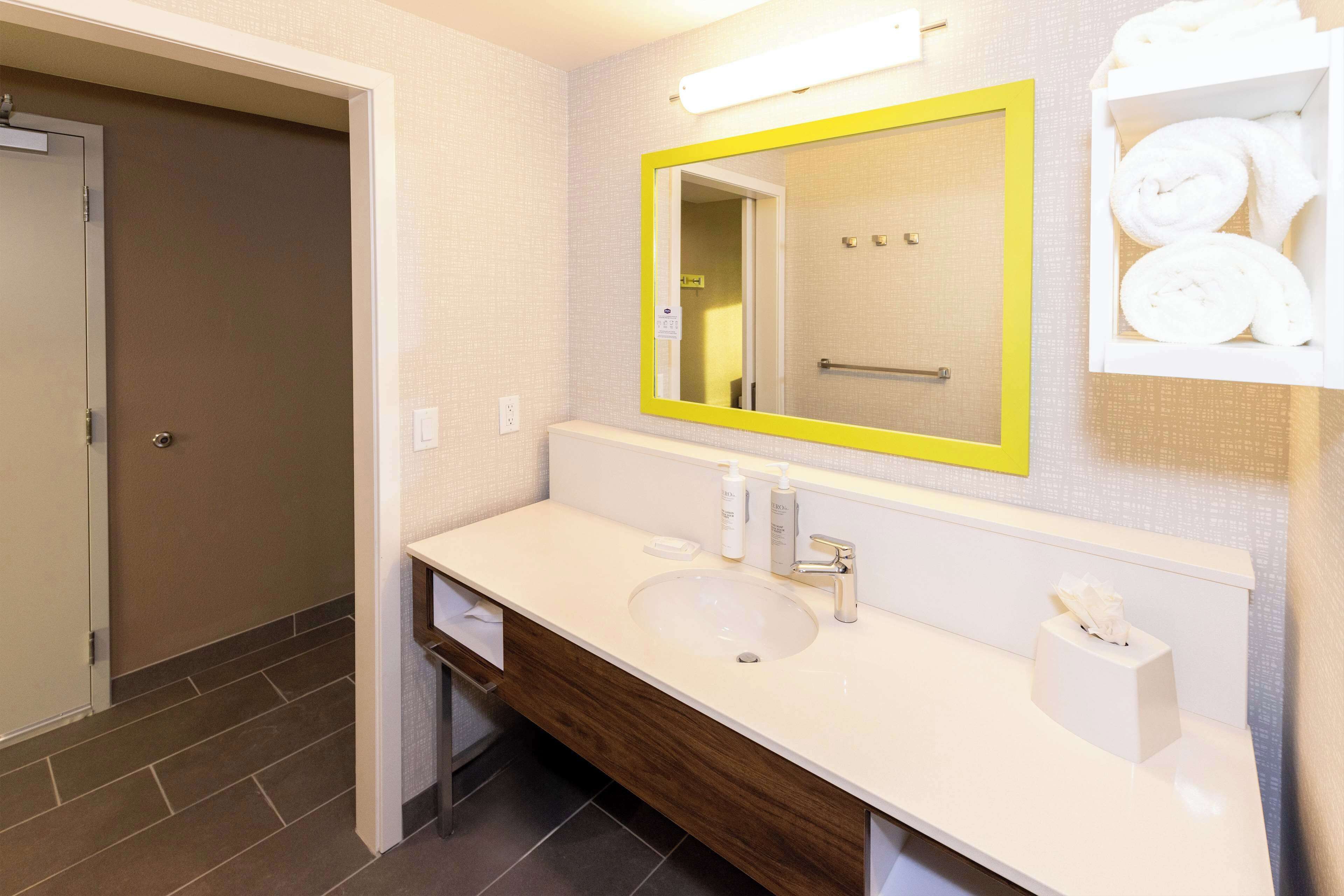 A bathroom with a white sink, a mirror with a yellow frame, and a towel rack with towels.