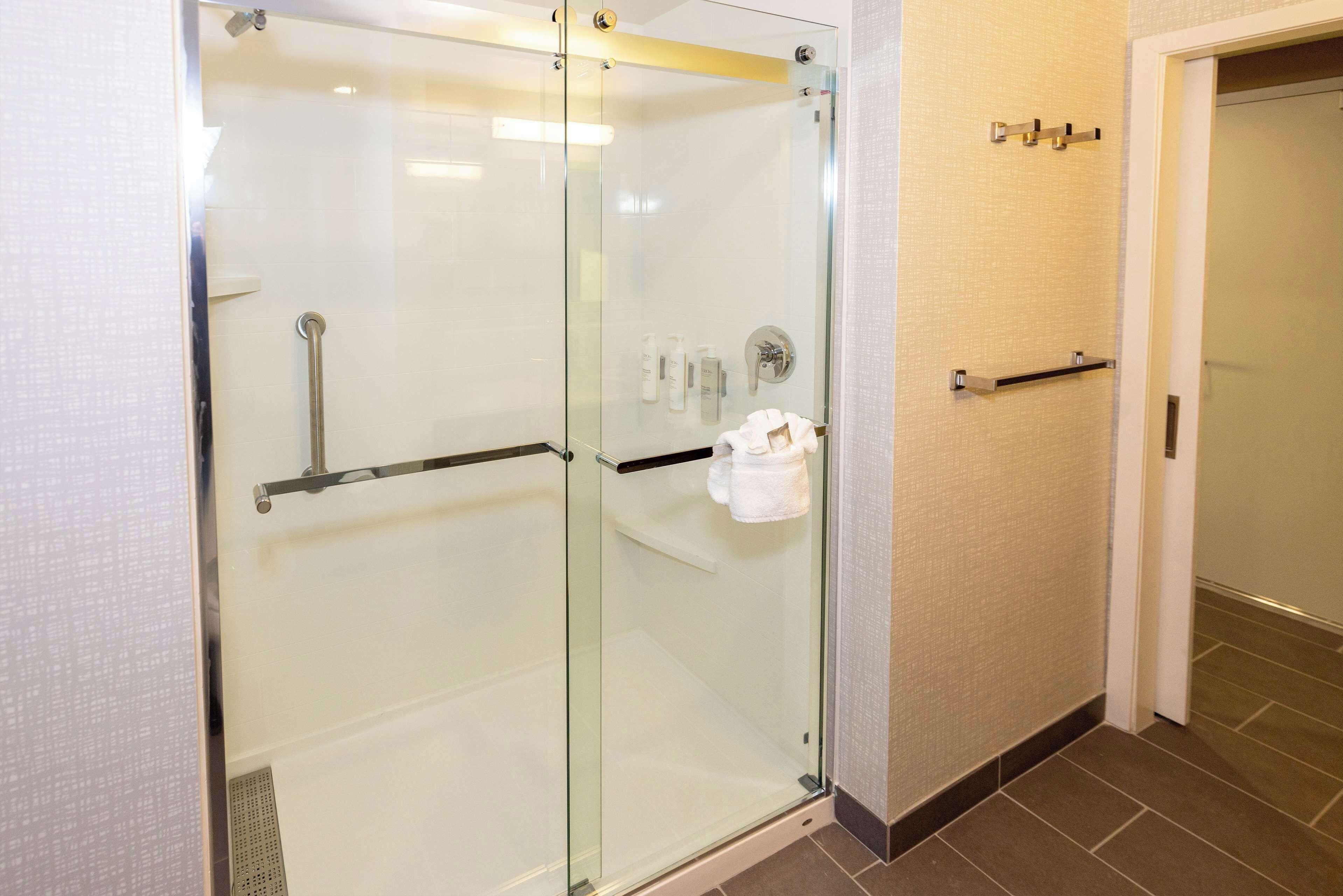 Une douche fermée par des parois en verre, dotée d’une barre d’appui, d’un porte-serviettes et d’une petite étagère pour les articles de toilette.