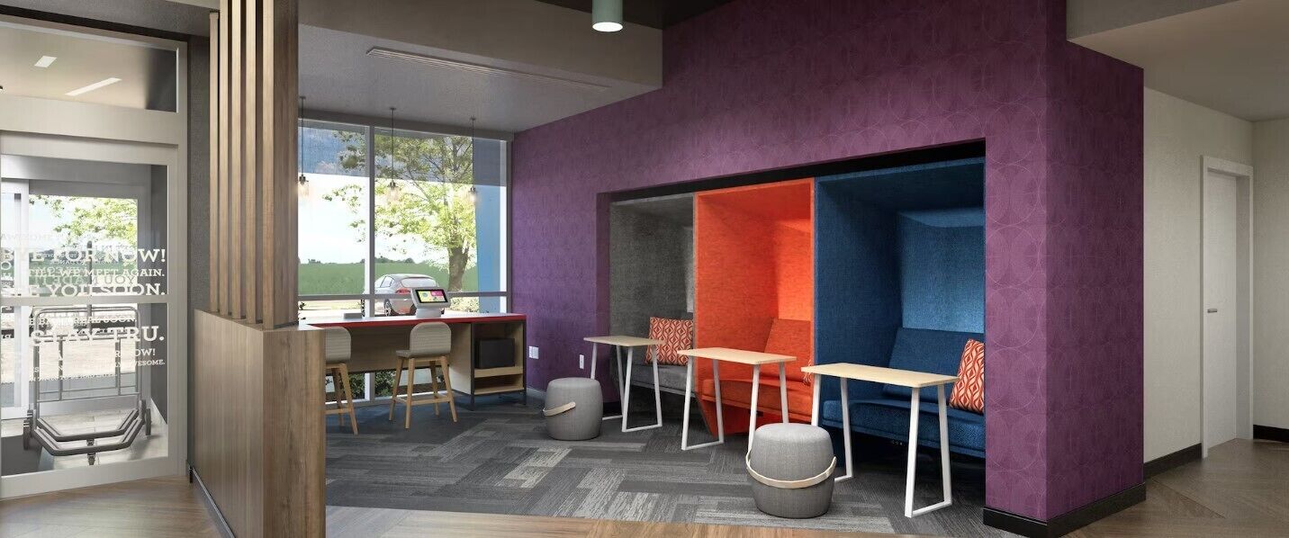 Un espacio de oficina moderno con pared de vidrio, un escritorio con computadora y una zona de estar con separador morado.