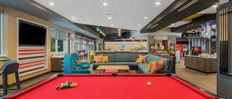 A pool table in a modern lounge area with a sofa and chairs, a bar, and a counter in the background.