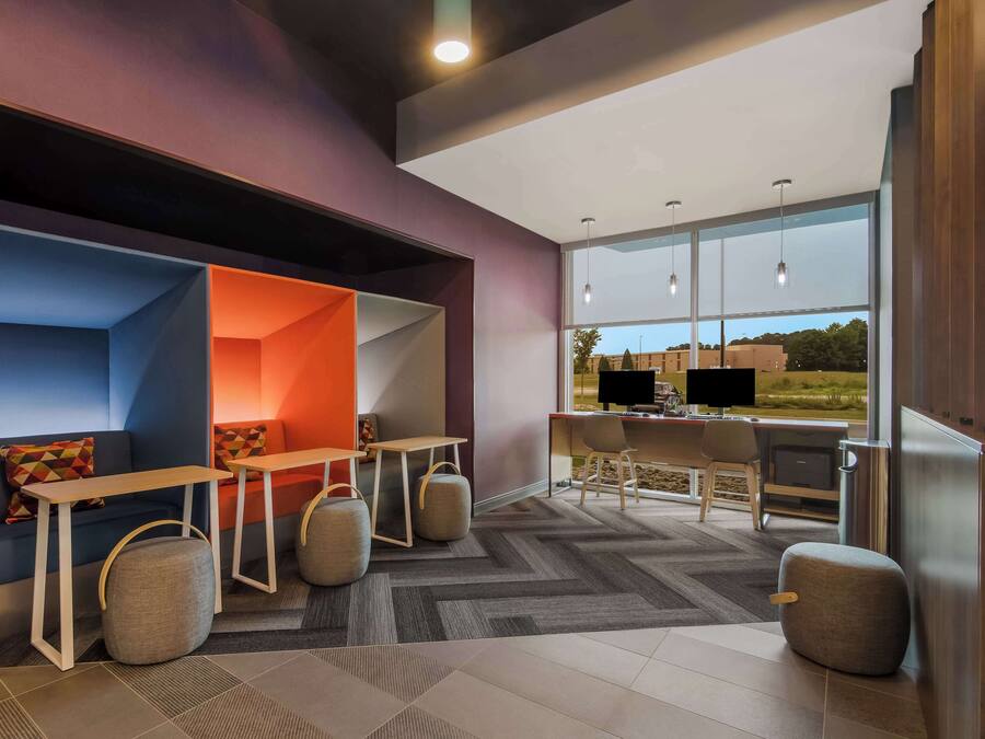 A modern office space with a sofa, tables, and chairs, a large window with a view, and a carpeted floor.