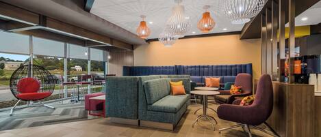 En moderne hotellobby med en hjørnesofa, et rundt bord og et barområde.