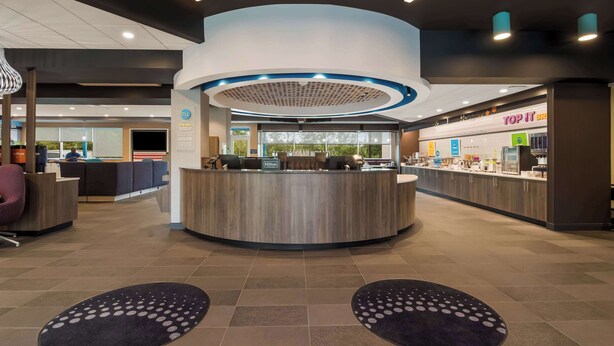 Een moderne hotellobby met een centraal receptiegedeelte, een zithoek en een zichtbaar restaurant genaamd 'TOP IT BRIO'.