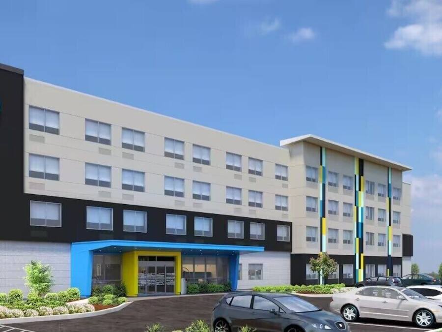 Um edifício de hotel moderno com uma placa chamativa 'tru by Hilton', vários andares e um estacionamento com vários carros.