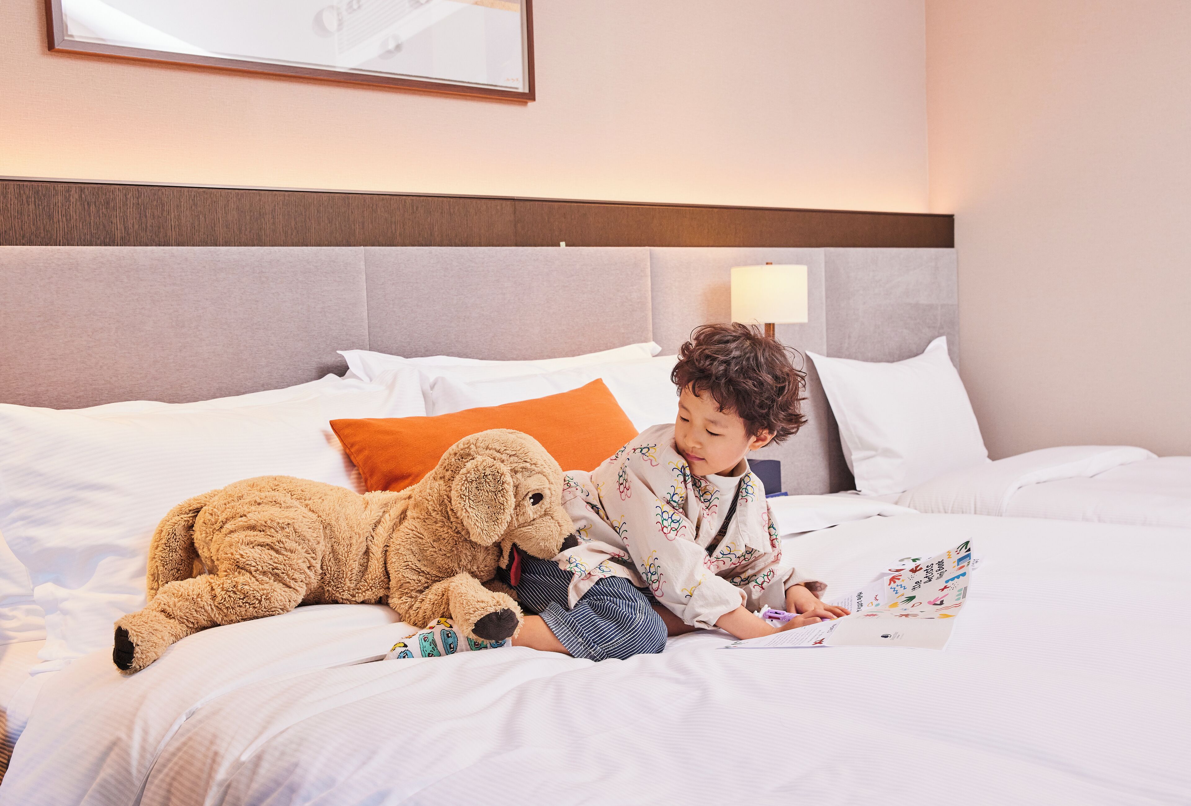 Un niño acostado en una cama con un peluche, leyendo un libro.