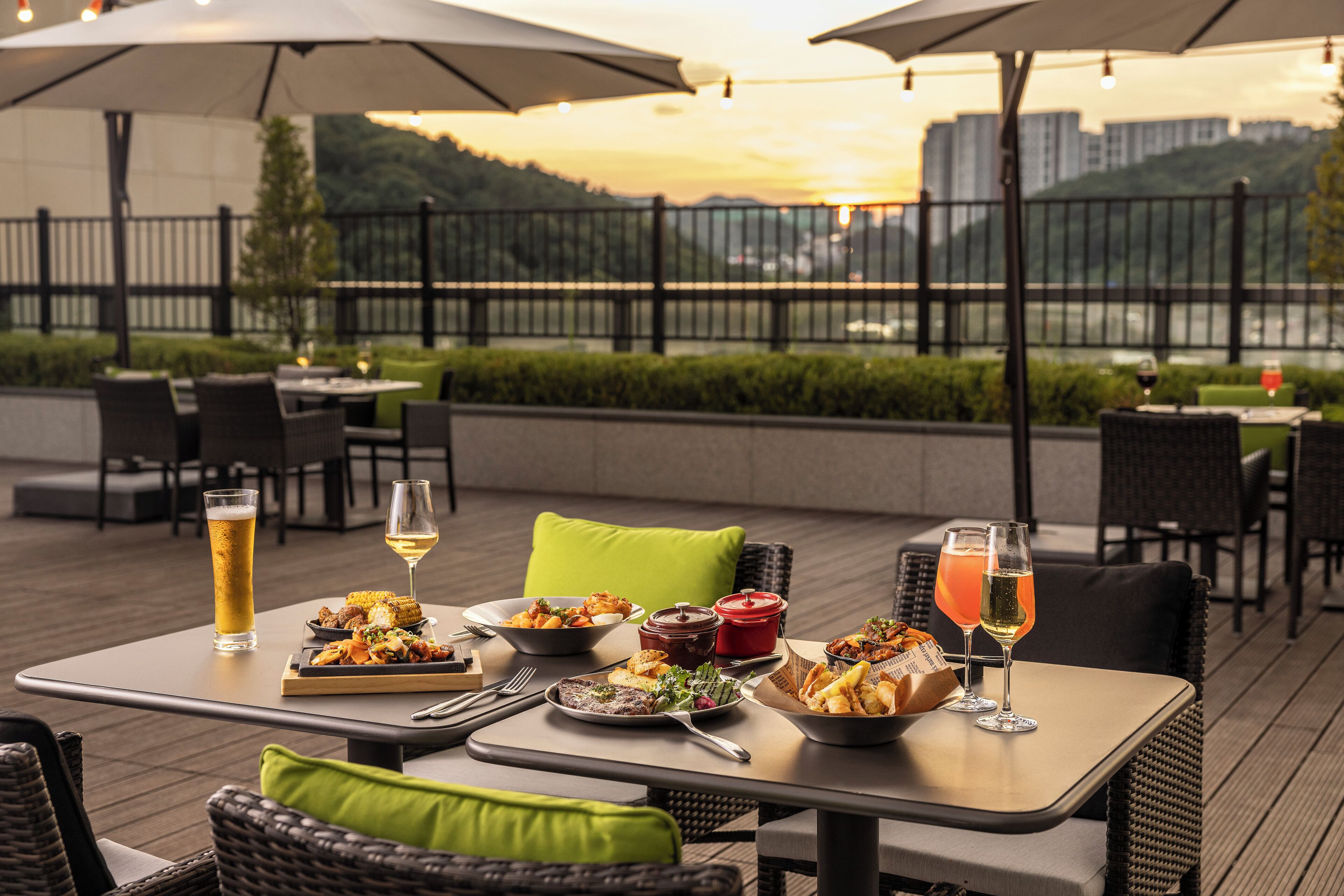 An outdoor dining area with tables, chairs, and umbrellas. There are plates of food and glasses of beverages on the tables.