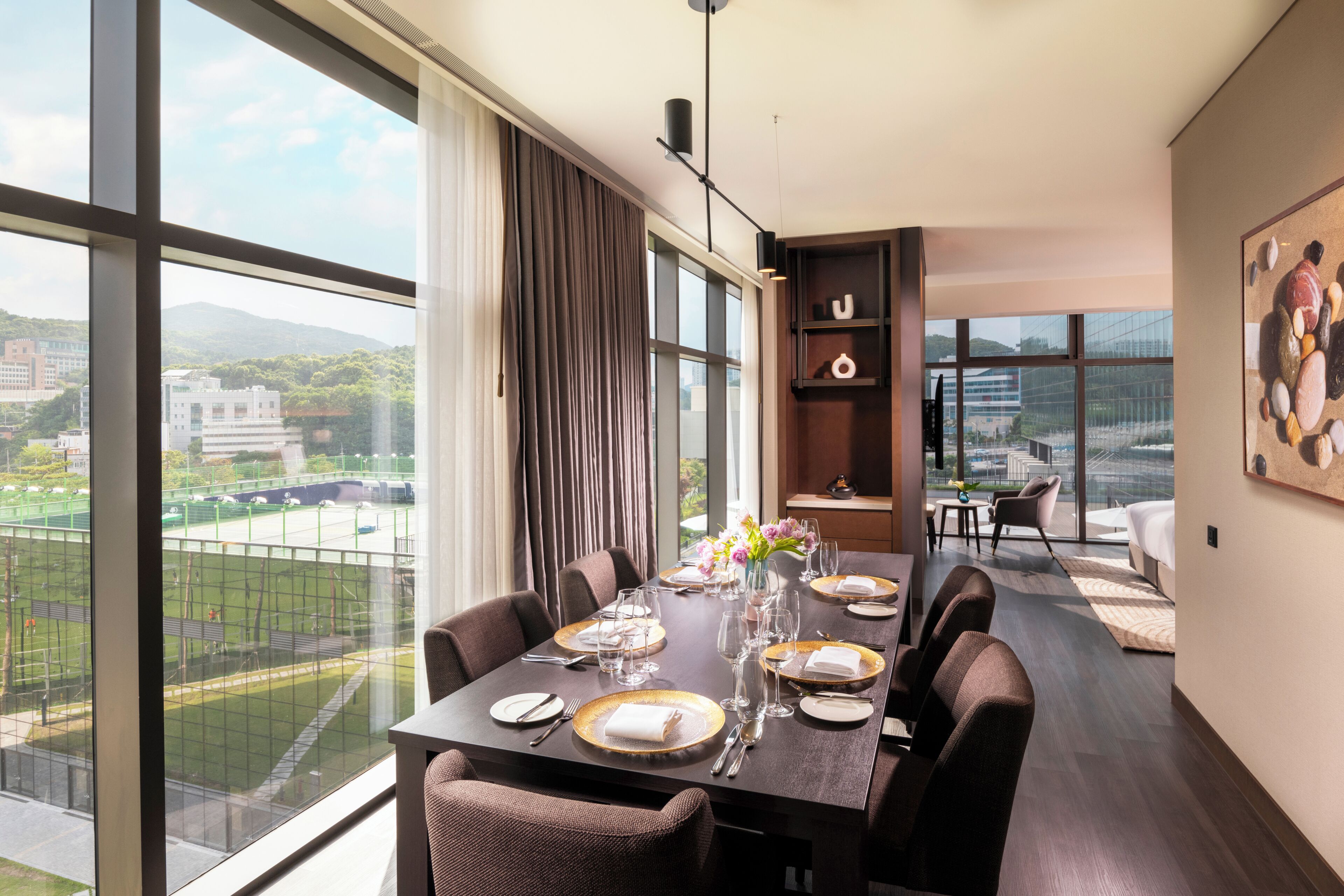 A modern dining area with a large table set for six, large windows, and a view of a cityscape.
