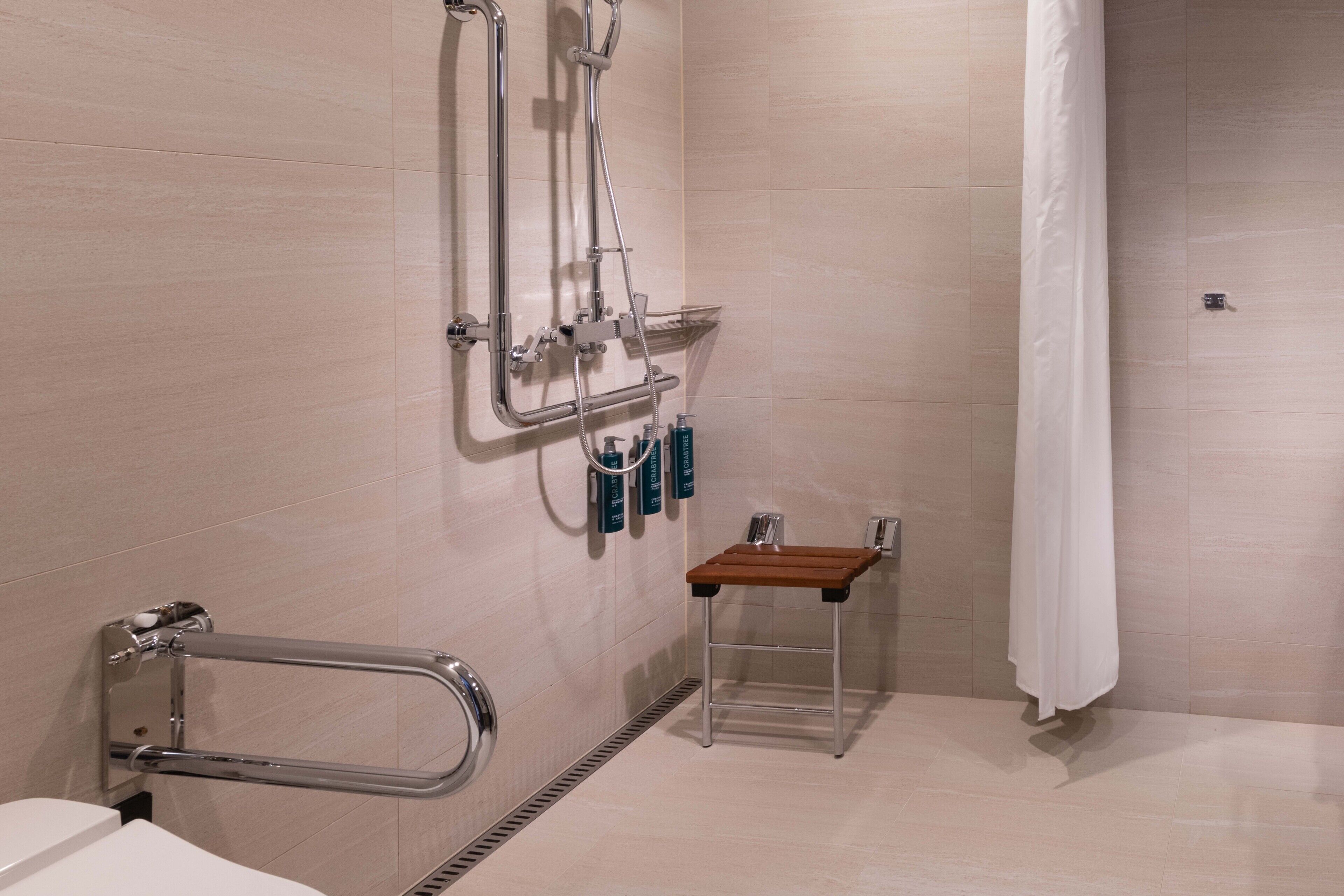 A bathroom with a shower, grab bars, a small table, and a towel rack.