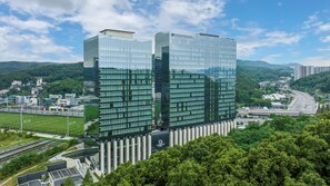 Un bâtiment moderne en verre, orné d’un logo bien visible, entouré d’une végétation luxuriante et se dressant sous un ciel dégagé.